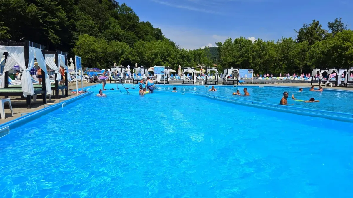 Piscină în aer liber și zonă de relaxare într-o zi însorită.